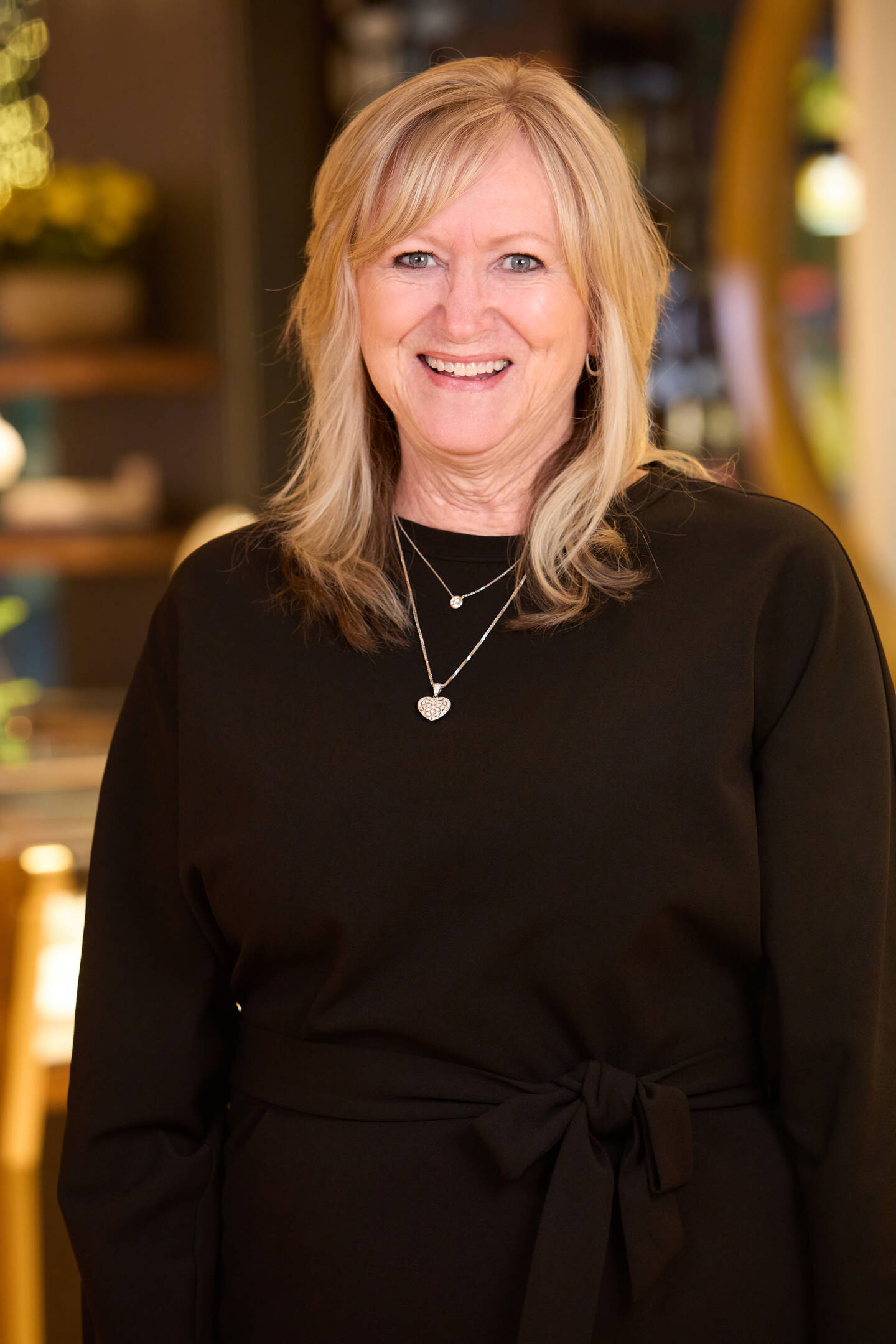 Laura Berringer smiling in a black shirt wearing gold necklaces. 
